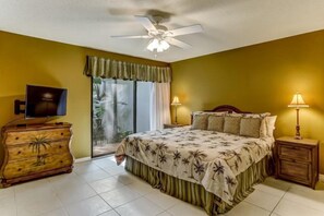 A bedroom with a bed, a television on a wooden dresser, two bedside lamps, and a ceiling fan.