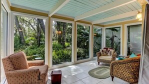 A sunroom with large windows, wicker furniture, and a tiled floor.