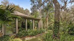 A modern glass house with a minimalist design, surrounded by lush greenery and trees.