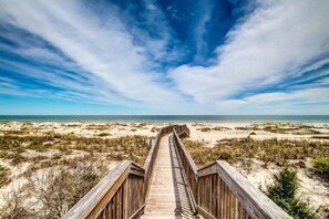 A wooden boardwalk leading to a beach with dunes and a clear sky. - 233-sandcastles (Fernandina Beach)