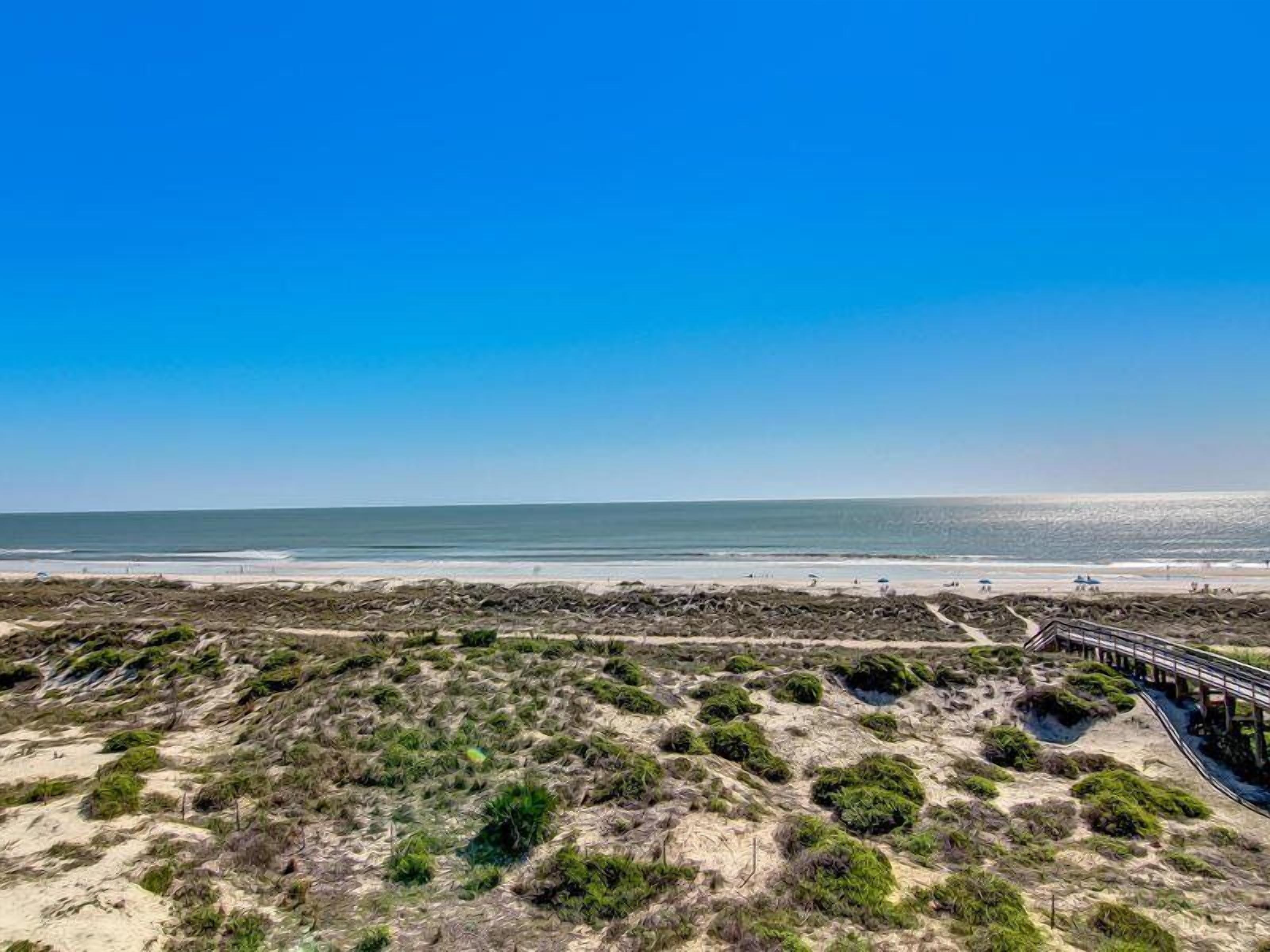 A beach with a wooden boardwalk leading to the water, sandy dunes, and sparse vegetation.