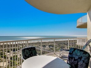A balcony with a view of the beach, white railing, and two chairs with floral upholstery. - 19-ocean-place (Fernandina Beach)