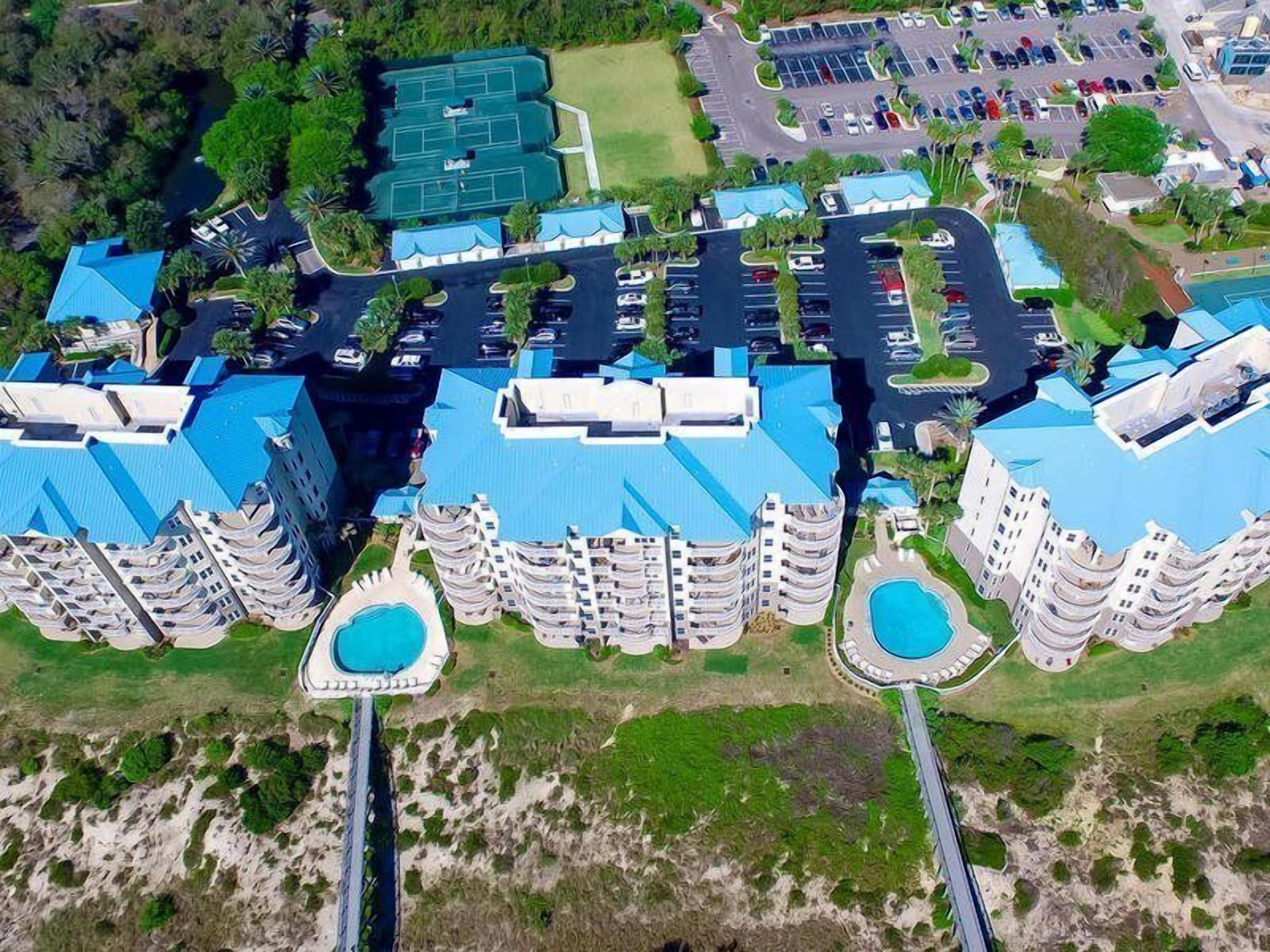 A high-rise hotel with multiple balconies, a central swimming pool, and a parking lot.