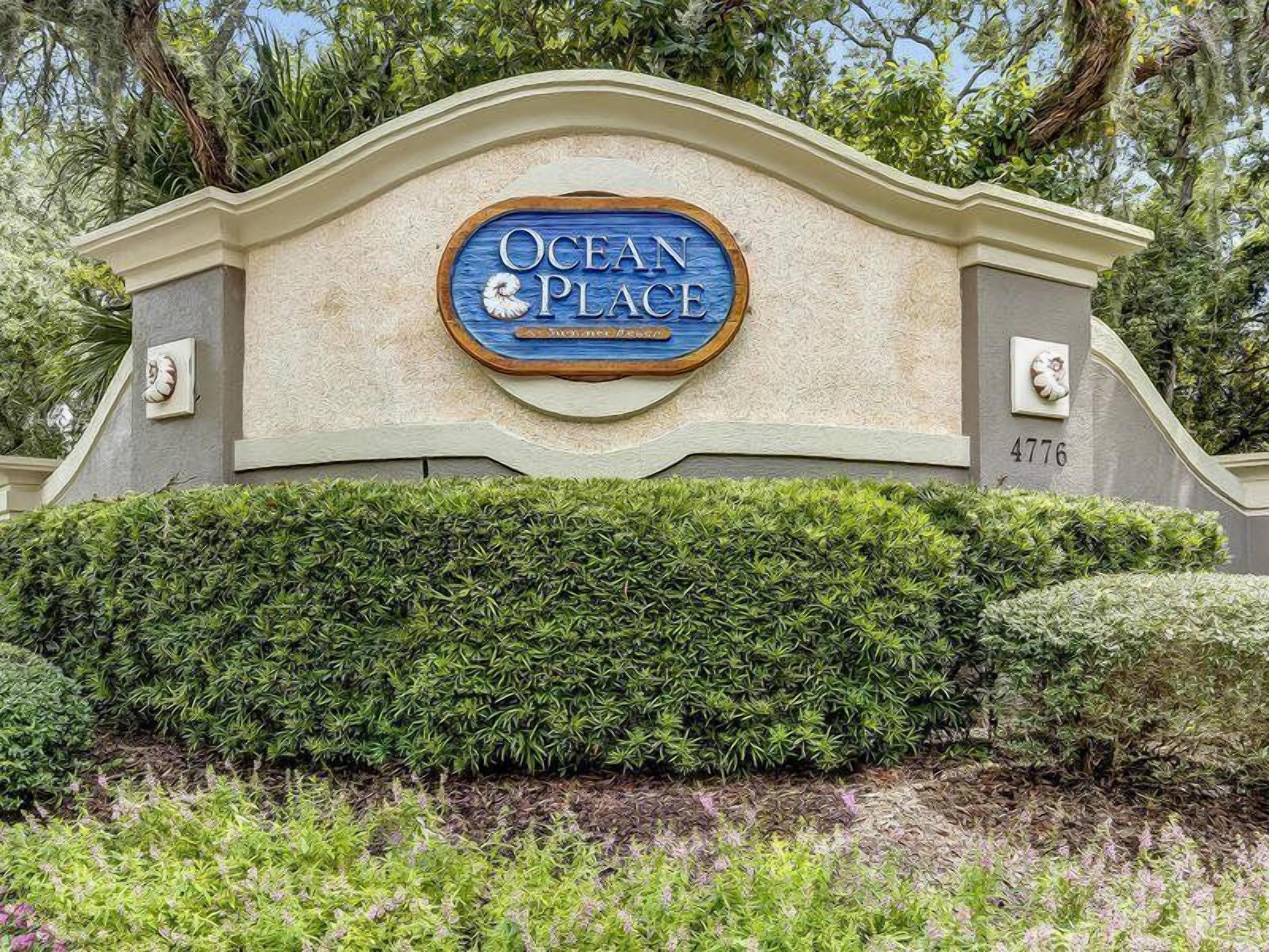 A sign with "Ocean Place" written on it, surrounded by greenery and a stone wall.