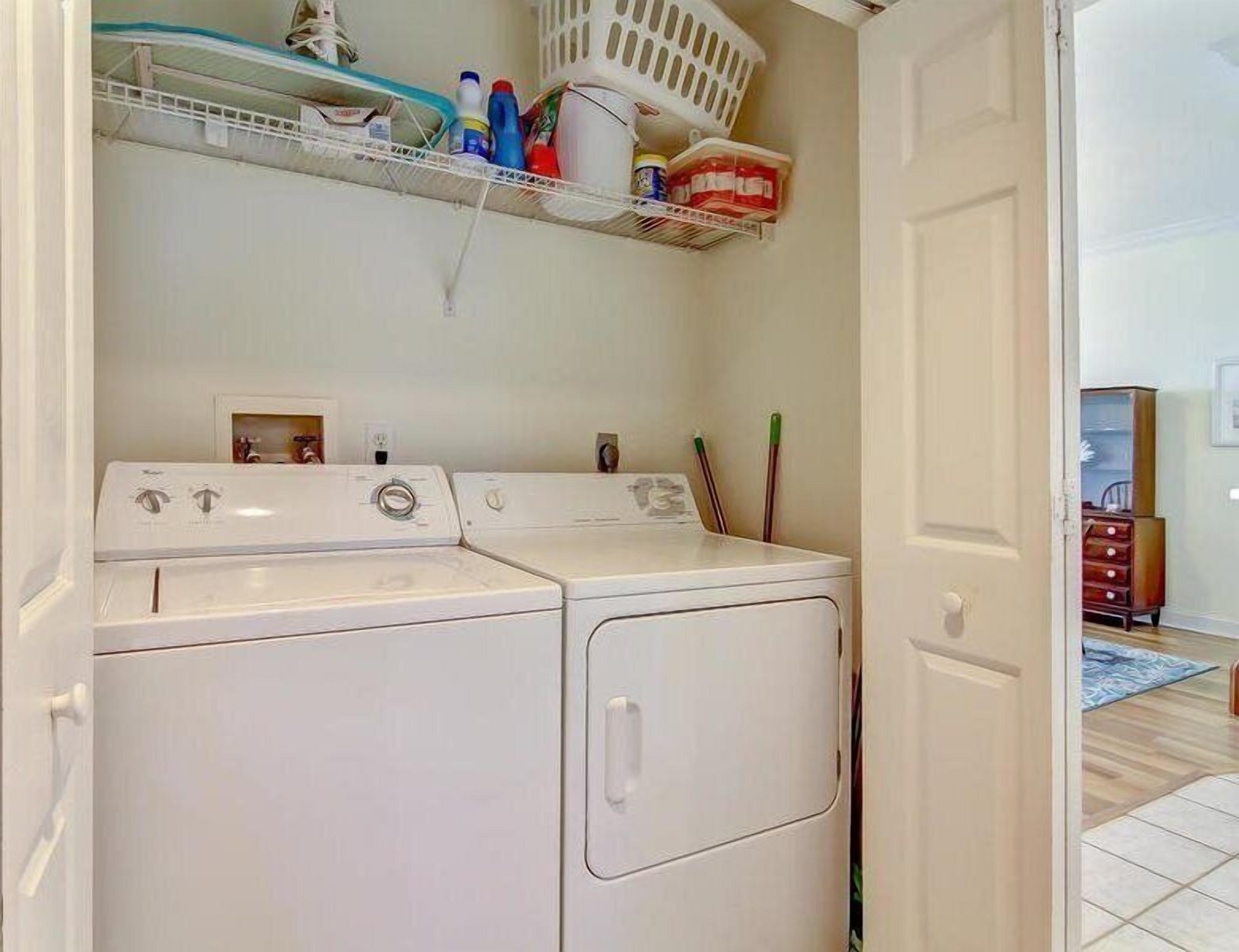 A laundry room with two stacked washers and dryers, a shelf with cleaning supplies, and a door leading to another room.