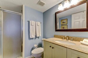 A bathroom with a shower, toilet, sink, and a large mirror. - 203-sailmaker (Fernandina Beach)