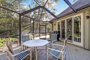 A covered patio with a table and chairs, a grill, and a view of the surrounding trees.