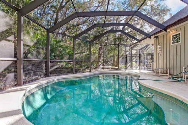 A swimming pool with a covered area, surrounded by trees and a house.