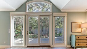 A room with a large sliding glass door leading to a backyard, a cushioned seating area, and a side table with a lamp. - 13-green-winged-teal (Fernandina Beach)