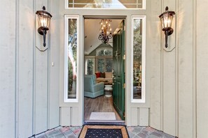 A hallway with a green door, a light-colored wall, and a chandelier.