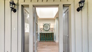 A hallway with a wooden floor leading to a room with a green patterned console table and a painting on the wall. - 13-green-winged-teal (Fernandina Beach)
