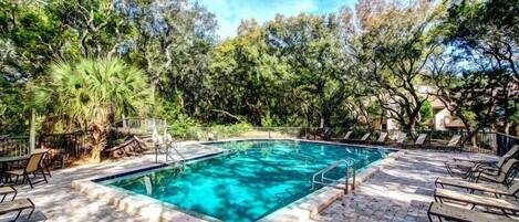 Una piscina rectangular con borde de azulejos, rodeada de sillas de descanso y un patio de ladrillo.