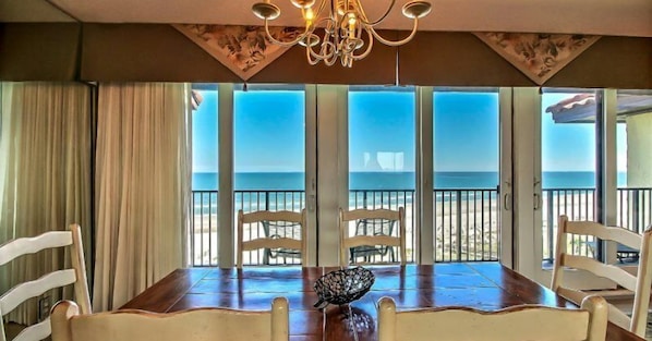 Enjoy meals with a view of the beach from this dining area, featuring a large table and comfortable seating for four.