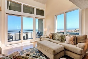 A spacious living room with a large sofa, a coffee table, and a view of the ocean through floor-to-ceiling windows. - 1180-beach-walker (Fernandina Beach)