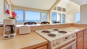 Una cocina moderna con estufa a gas, cafetera y vistas al océano a través de amplios ventanales.