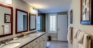 A bathroom with two sinks, a large mirror, and a door leading to another room. - 1801-turtle-dunes (Fernandina Beach)