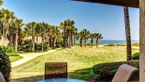 A view of a golf course with a clear sky, palm trees, and a distant ocean. - 1801-turtle-dunes (Fernandina Beach)