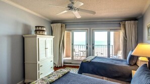A bedroom with two beds, a ceiling fan, a wardrobe, and a balcony with a view.