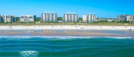 A beachfront hotel with multiple floors, a sandy beach, and ocean waves.