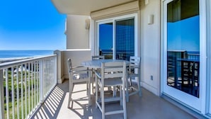 A balcony with a table and chairs, a view of the ocean, and a sliding glass door. - 12-ocean-place (Fernandina Beach)