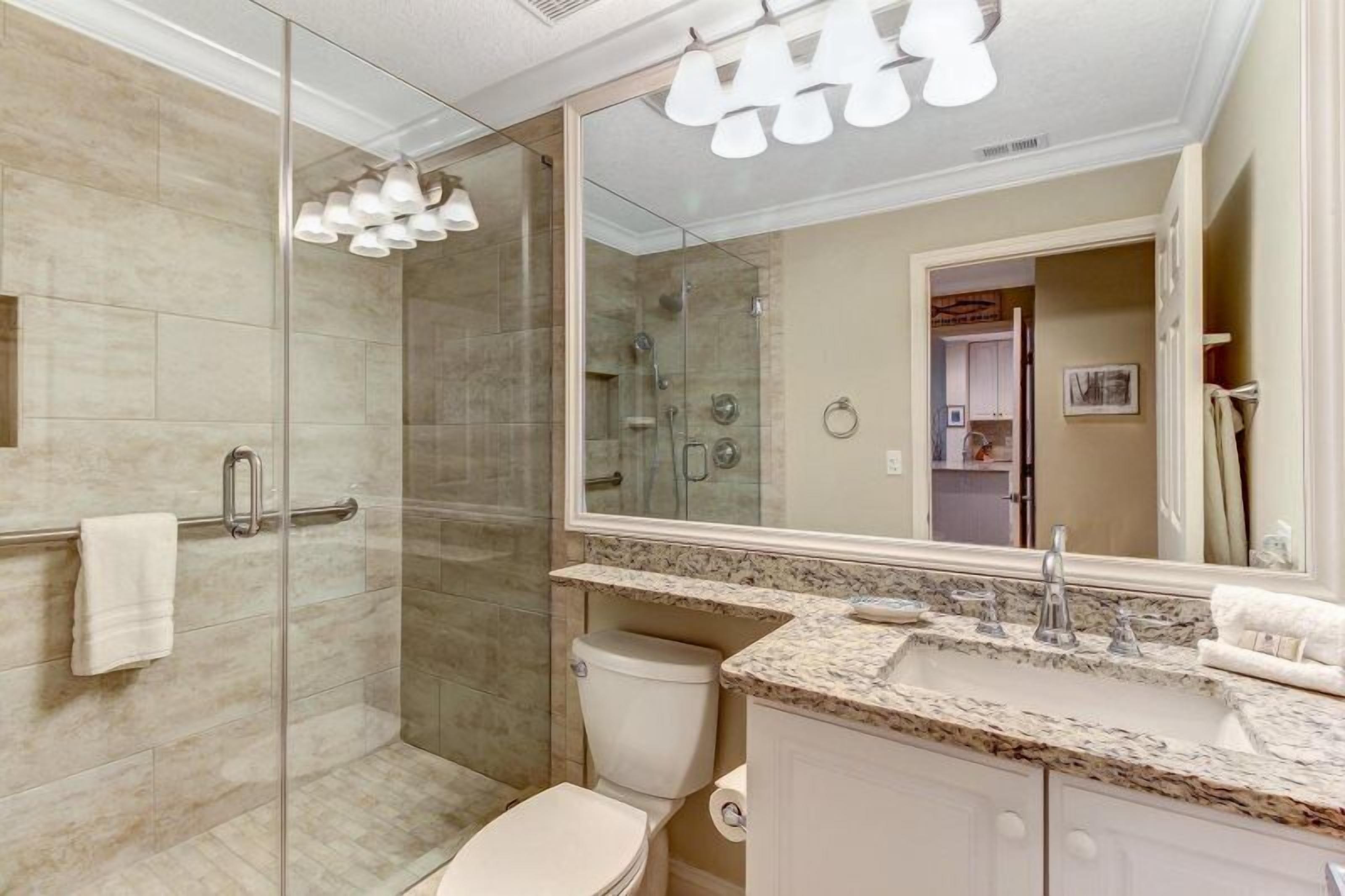 A modern bathroom with a glass-enclosed shower, a vanity with a marble countertop, and a large mirror.