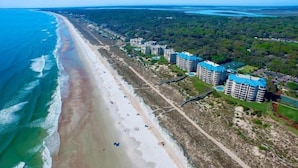 An aerial view of a coastal area with a beach, a road, and several multi-story buildings with blue roofs. - 12-ocean-place (Fernandina Beach)