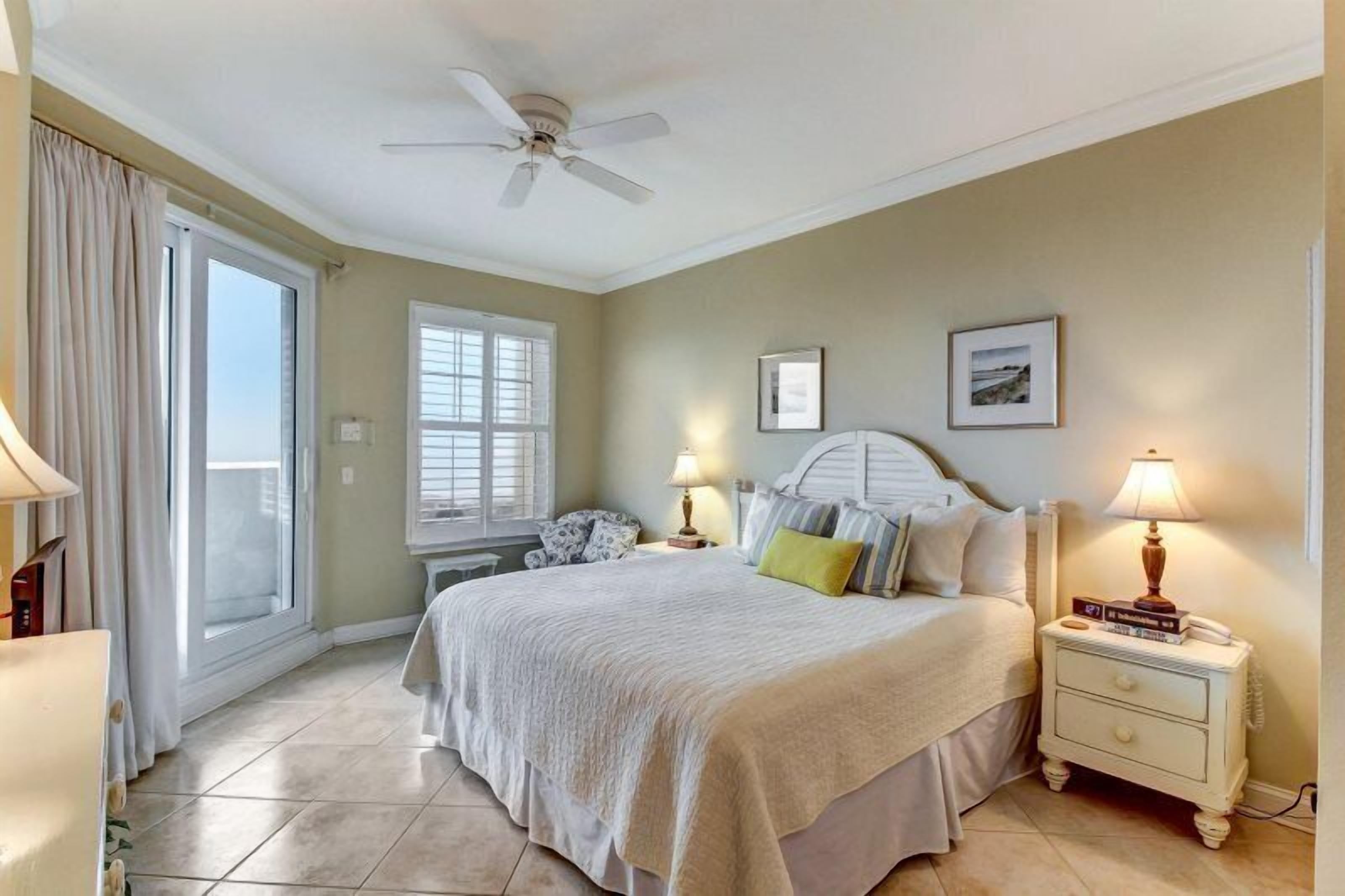 Un dormitorio con cama, lámparas de noche, mesita de noche, ventilador de techo y ventana con cortinas.