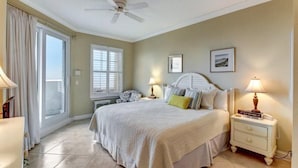 A bedroom with a bed, bedside lamps, a nightstand, a ceiling fan, and a window with curtains. - 12-ocean-place (Fernandina Beach)