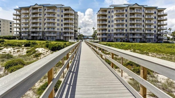 A wooden boardwalk leading to a beachfront apartment complex with multiple balconies. - 12-ocean-place (Fernandina Beach)