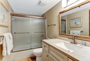 A bathroom with a glass-enclosed shower, a white sink, and a large mirror.