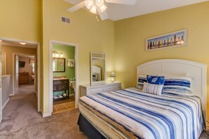 A bedroom with a large bed, a dresser, a vanity with a mirror, and a ceiling fan.