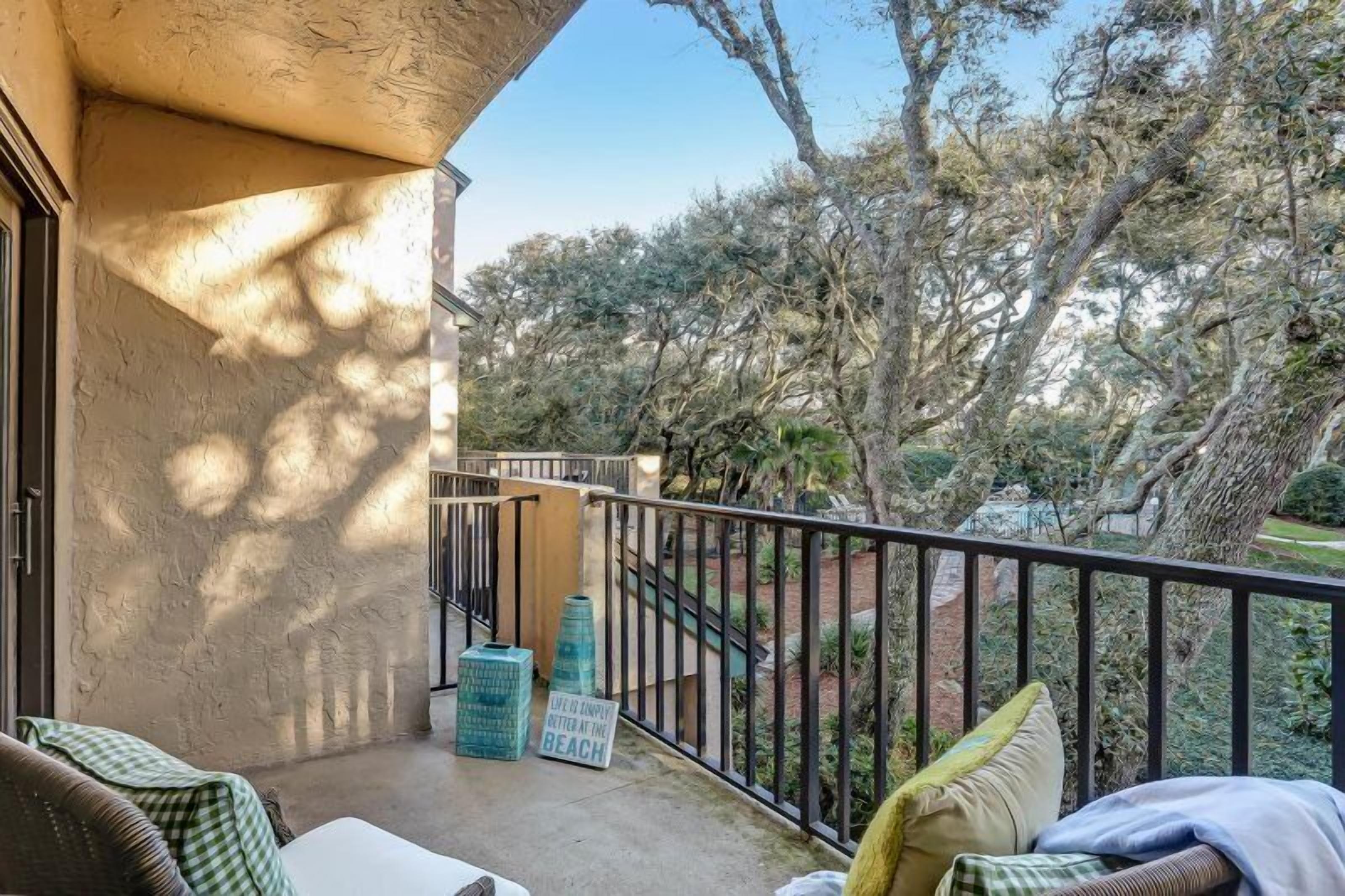 A balcony with wicker furniture, a concrete floor, and a view of trees and a garden.