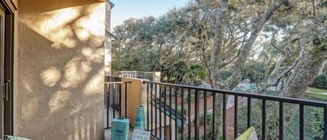 A balcony with wicker furniture, a concrete floor, and a view of trees and a garden.