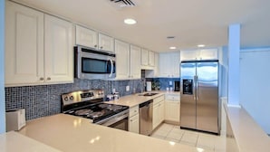 A modern kitchen with white cabinets, a stainless steel refrigerator, a microwave, and a stove. - 1354-shipwatch (Fernandina Beach)