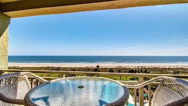 A balcony with wicker chairs and a glass-top table overlooking a beach. - 1354-shipwatch (Fernandina Beach)