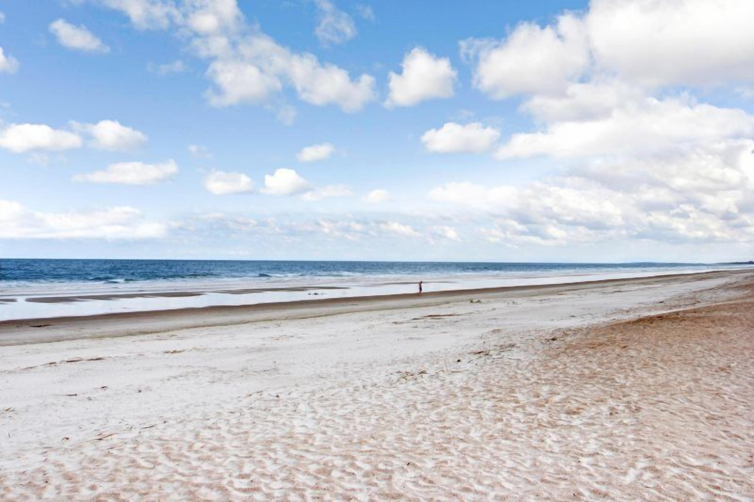 Una playa con una amplia orilla de arena y el océano al fondo.