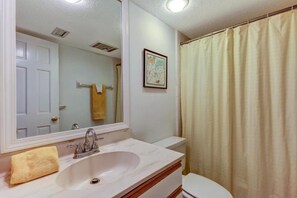 Un bagno con lavandino bianco, specchio, WC e tenda doccia.