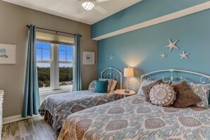 A bedroom with two beds, a window with curtains, star decorations on the wall, and a lamp on a bedside table. - 60-ocean-place (Fernandina Beach)