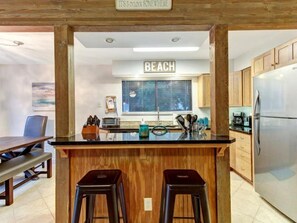 A kitchen with wooden cabinets, a stainless steel refrigerator, a countertop with a sink, and a sign that reads "BEACH". - 2594 Forest Ridge Drive (Fernandina Beach)