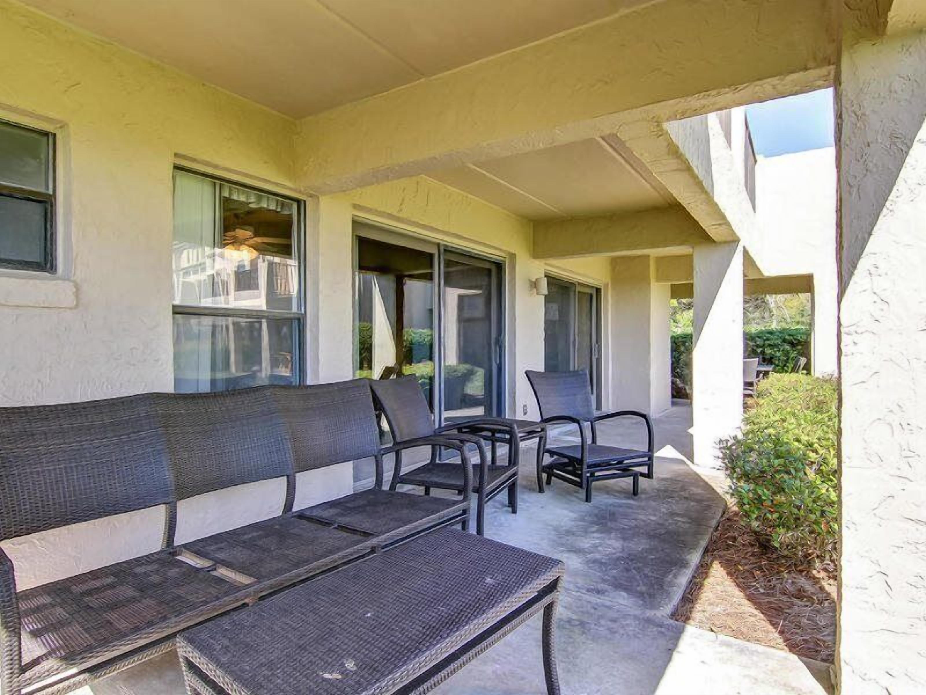 An outdoor seating area with a bench and chairs, a covered patio, and a building entrance.