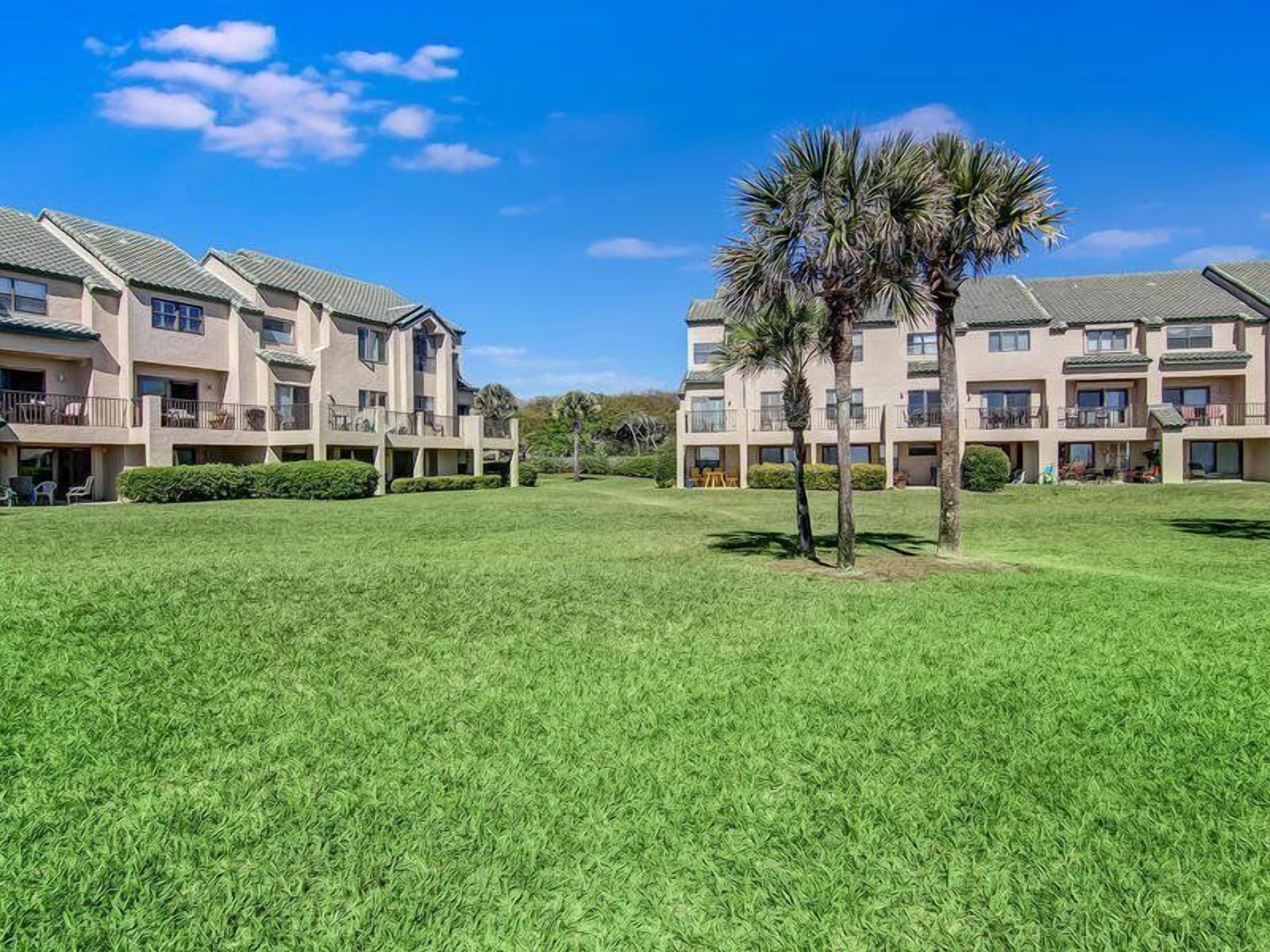 A multi-story hotel with a central courtyard featuring palm trees and well-maintained grass.