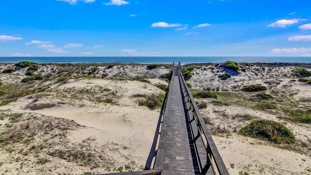 A wooden boardwalk leading to a beach with dunes and sparse vegetation. - 204-sailmaker (Fernandina Beach)