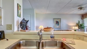 A kitchen with a double stainless steel sink, a refrigerator, and a microwave. There is a decorative fish sculpture on the counter, and a painting on the wall. - 204-sailmaker (Fernandina Beach)