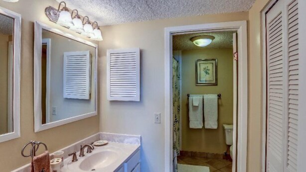 Une salle de bain avec un lavabo, un miroir et un porte-serviettes. Une porte donne accès à une autre pièce.