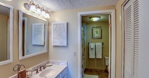 A bathroom with a sink, mirror, and towel rack. There is a door leading to another room. - 1825-turtle-dunes (Fernandina Beach)