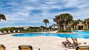 Un espace piscine avec des chaises longues, des palmiers et un bâtiment en arrière-plan.