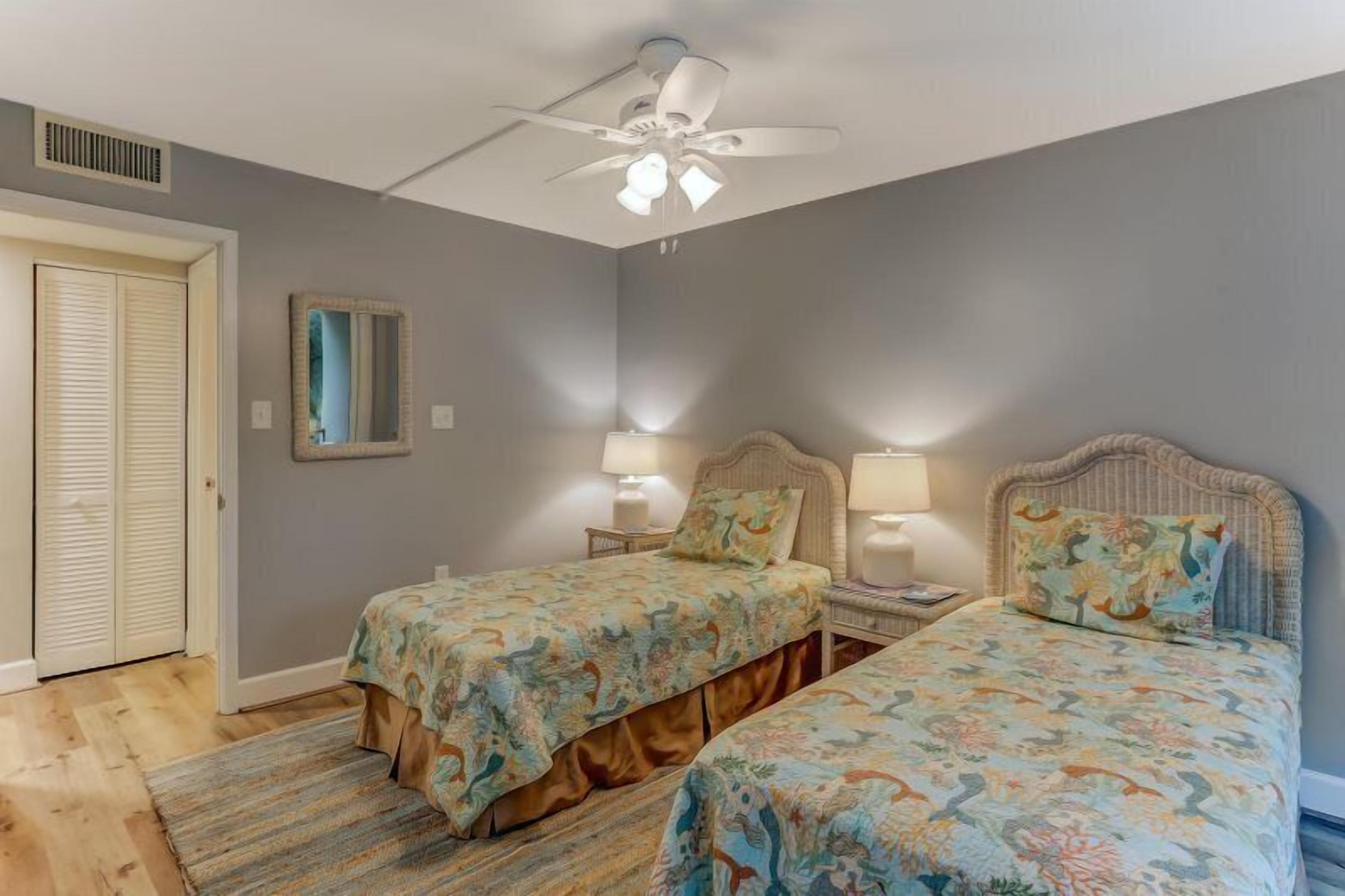 Quarto com duas camas, um ventilador de teto e um espelho na parede.