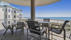 A balcony with a table and chairs, overlooking a beach and a building with multiple windows. - 61-ocean-place (Fernandina Beach)