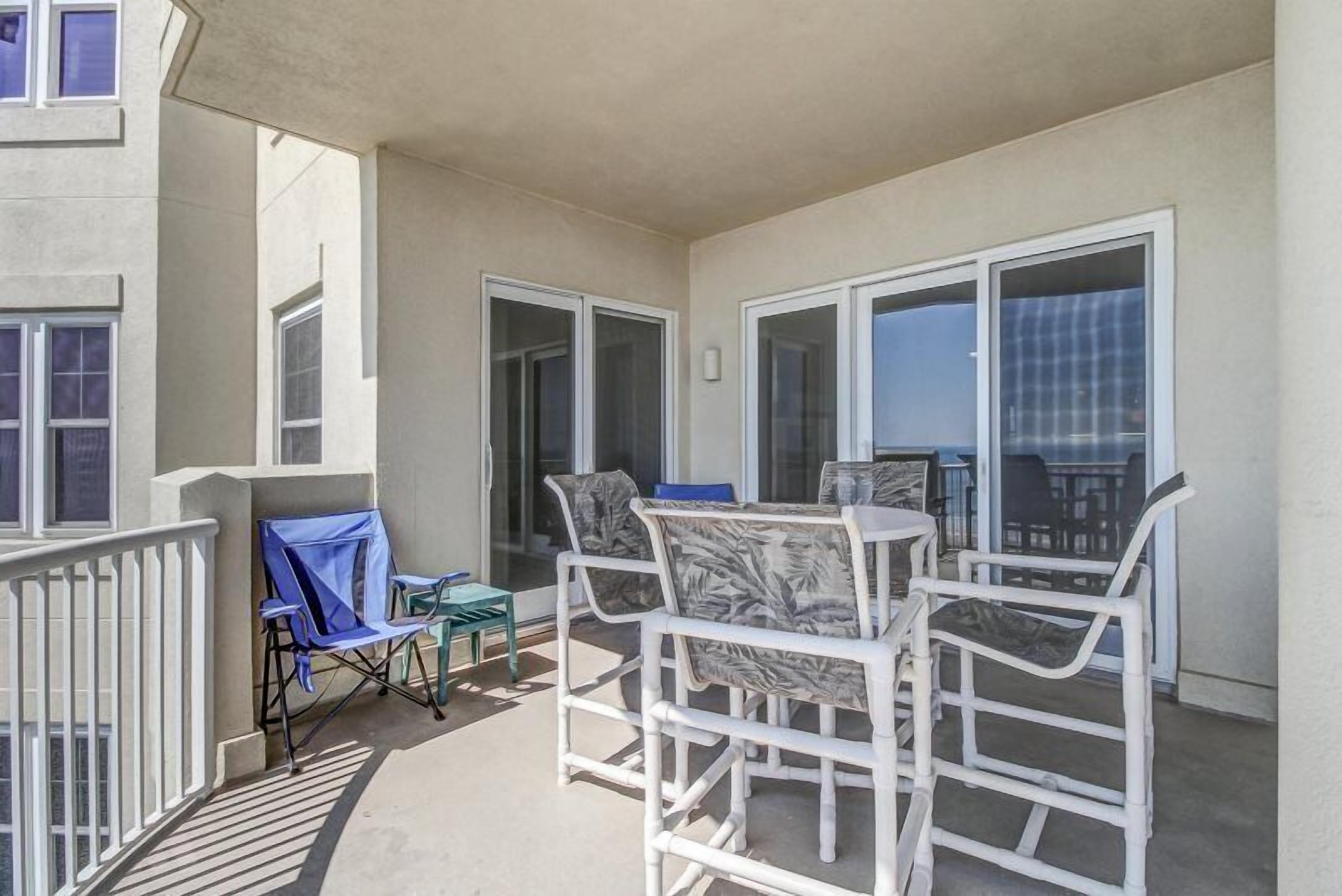 A balcony with white wicker furniture, a blue folding chair, and a small table.