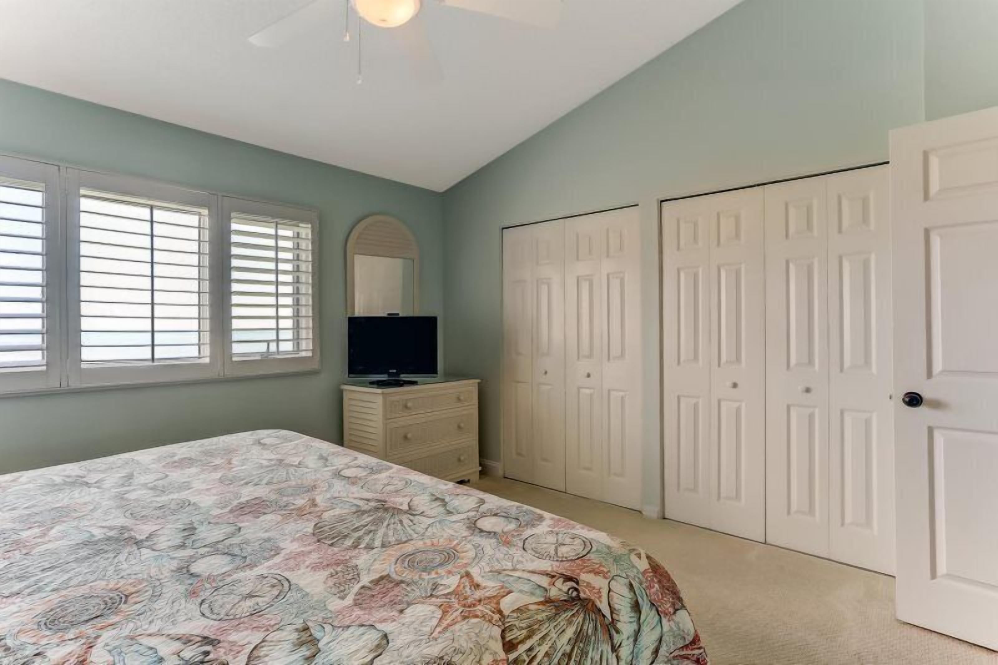 A bedroom with a bed, dresser, TV, and closet.
